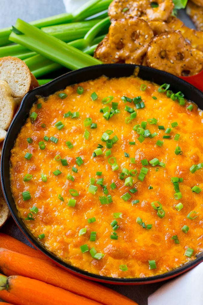 Buffalo Ranch Chicken Dip | Buffalo Chicken Dip | Baked Buffalo Dip | Cheesy Buffalo Dip #buffalowings #buffalochicken #dip #lowcarb #appetizer #sraye Buffalo ranch chicken dip topped with melted cheese and green onions, surrounded by vegetables, pretzels and baguette slices.