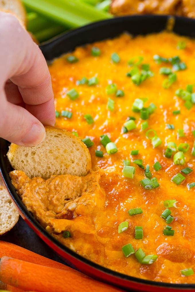 Buffalo Ranch Chicken Dip | Buffalo Chicken Dip | Baked Buffalo Dip | Cheesy Buffalo Dip #buffalowings #buffalochicken #dip #lowcarb #appetizer #sraye Baked buffalo chicken dip with a baguette slice scooping some out.