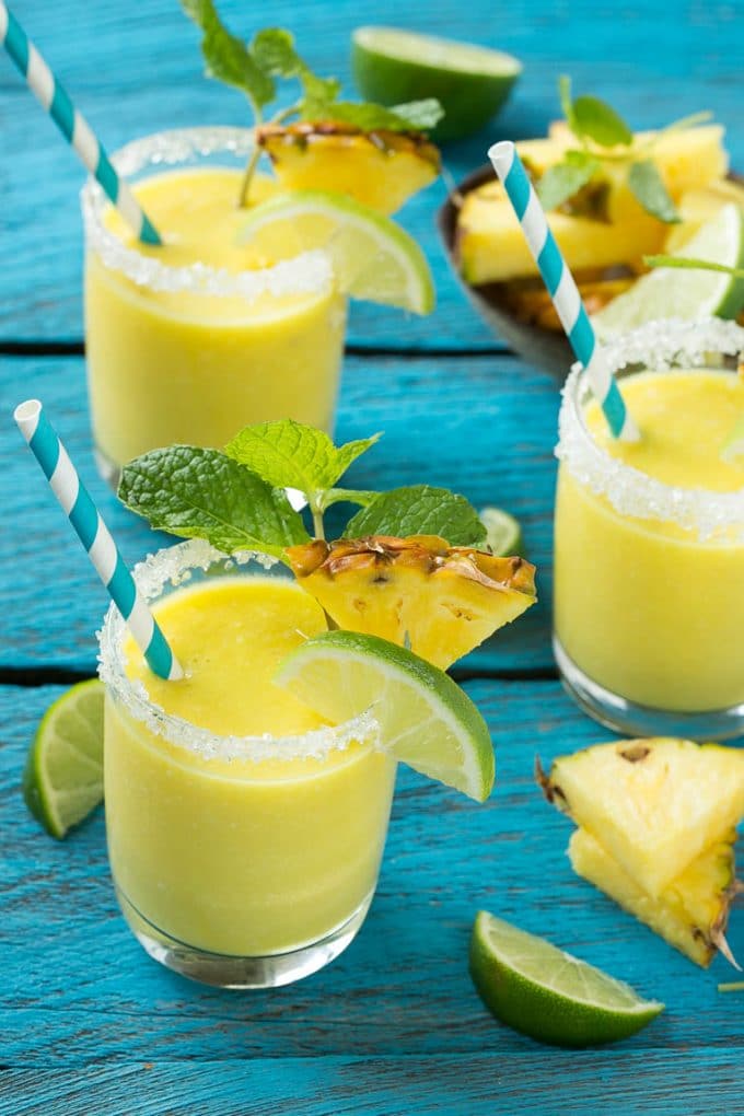 Pineapple Coconut Smoothie Recipe |Tropical Smoothie | Pineapple Smoothie #smoothie #pineapple #coconut #healthy #cleaneating #sraye Glasses of pineapple coconut smoothie garnished with limes and mint.