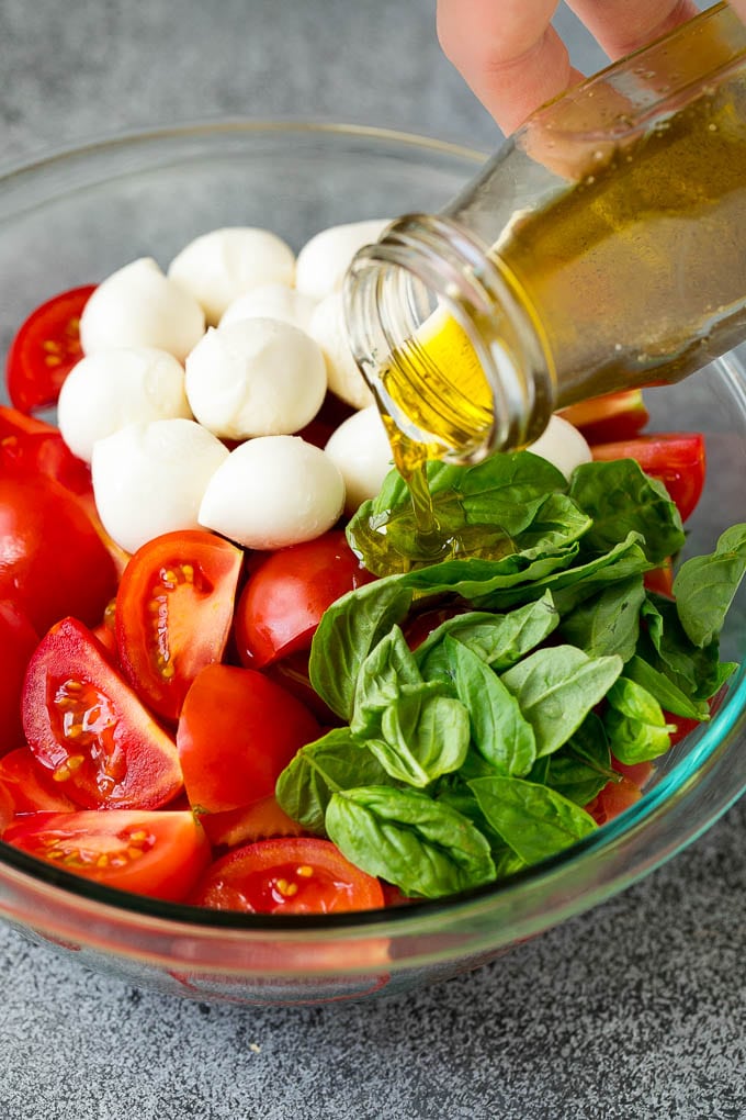 Caprese Salad Recipe | Tomato Salad #salad #tomato #mozzarella #cheese #basil #caprese #summer #sraye Olive oil being poured over tomatoes, mozzarella and basil leaves.