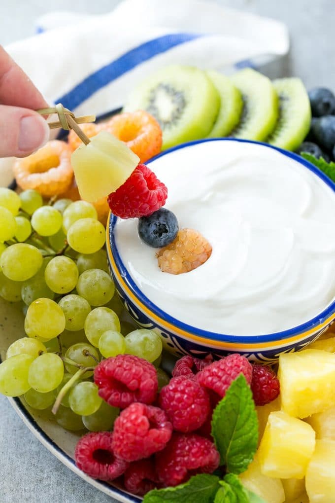 Cream Cheese Fruit Dip | Fruit Recipe | Fruit Dip #fruit #dip #creamcheese #snack #dessert #sraye A skewer of berries going into a bowl of fruit dip.
