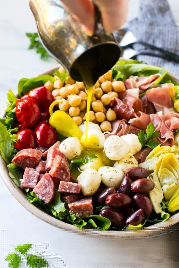 Antipasto Salad Recipe | Italian Salad | Main Course Salad | Antipasto Recipe #salad #salami #italianfood #dinner #lunch #sraye A pitcher of dressing being poured over antipasto salad.