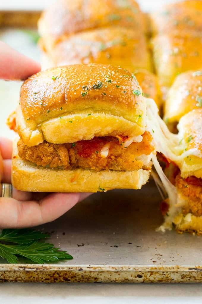 Chicken Parmesan Sliders | Chicken Parmesan Sandwich Recipe | Slider Sandwich Recipe #sliders #chickenparm #chickenparmesan #chickenparmesansliders #dinner #appetizer #sraye A crispy chicken parmesan slider being pulled away by a hand.