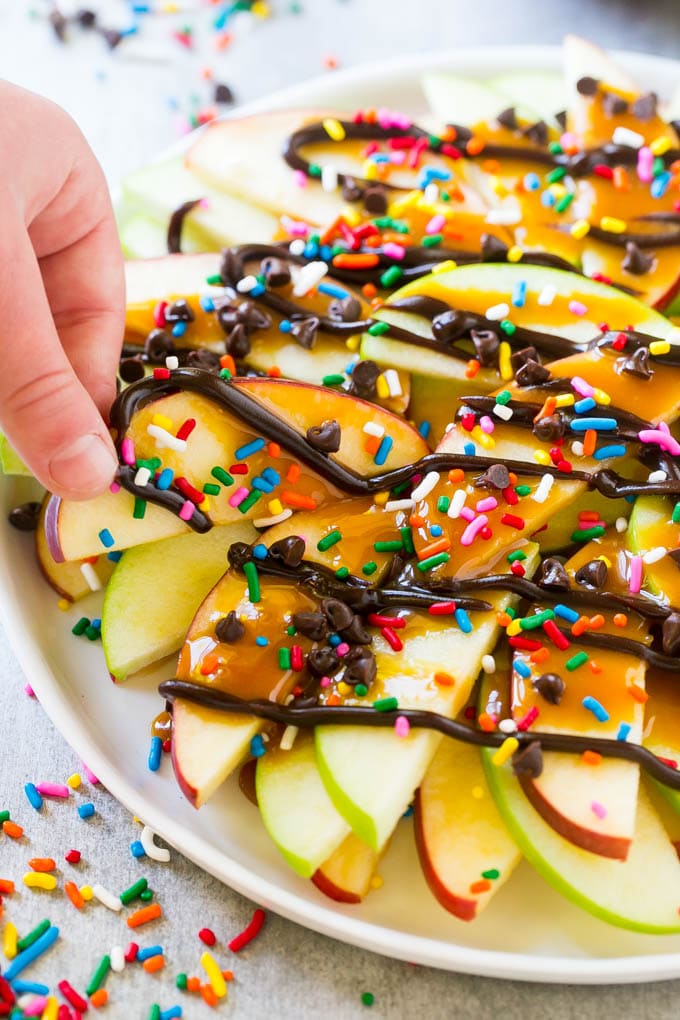 Apple Nachos Recipe | After School Snack | Caramel Apples #apple #apples #caramelapple #snack #dessert #sraye A plate of caramel apple nachos with a hand reaching out to take one.