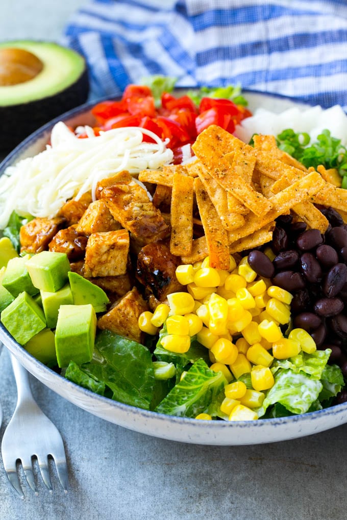 BBQ Chicken Salad Recipe | Chopped BBQ Chicken Salad | CPK Copycat Recipe | California Pizza Kitchen Copycat Recipe | Chicken Ranch Salad #copycat #CPK #BBQchicken #chicken #salad #dinner #sraye A bowl of salad topped with chicken, tortilla strips, black beans, jiacama, avocado and tomatoes.