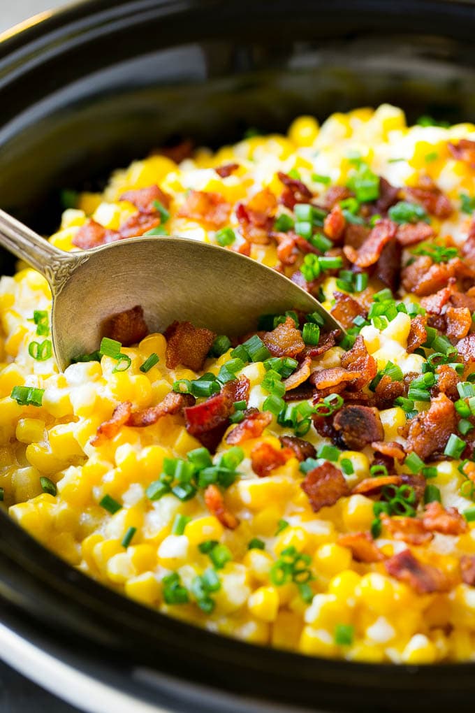 Slow Cooker Creamed Corn Recipe | Easy Creamed Corn Recipe | Slow Cooker Creamed Corn with Bacon | Southern Creamed Corn | Creamed Corn with Cream Cheese #creamedcorn #corn #bacon #crockpot #slowcooker #dinner #sraye A serving spoon in a crock pot full of creamed corn.
