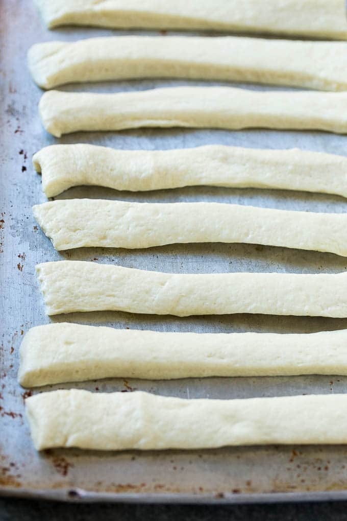 Garlic Knots Recipe | Garlic Rolls | Garlic Butter Rolls | Garlic Bread Recipe #garlic #garlicbread #garlicknots #breadsticks #sraye Strips of pizza dough on a sheet pan that are ready to be tied up.
