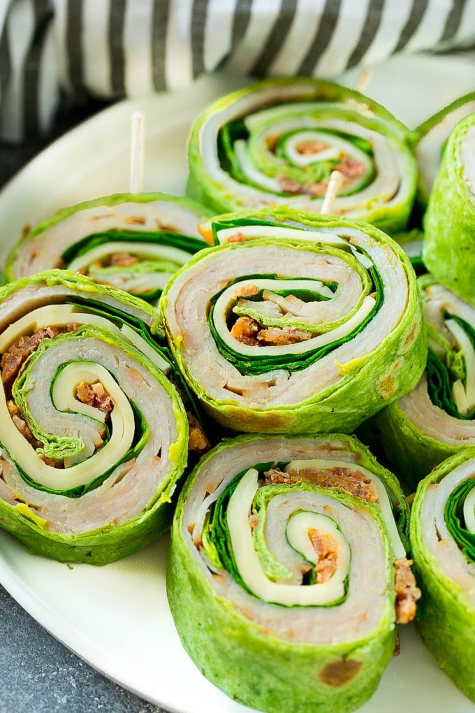 Turkey Roll Ups Recipe | Turkey Pinwheel Sandwiches | Turkey Roller Sandwiches #turkey #avocado #sandwich #lunch #appetizer #sraye Turkey roll up sandwiches filled with cheese, avocado, bacon, turkey and spinach and stacked on a plate.