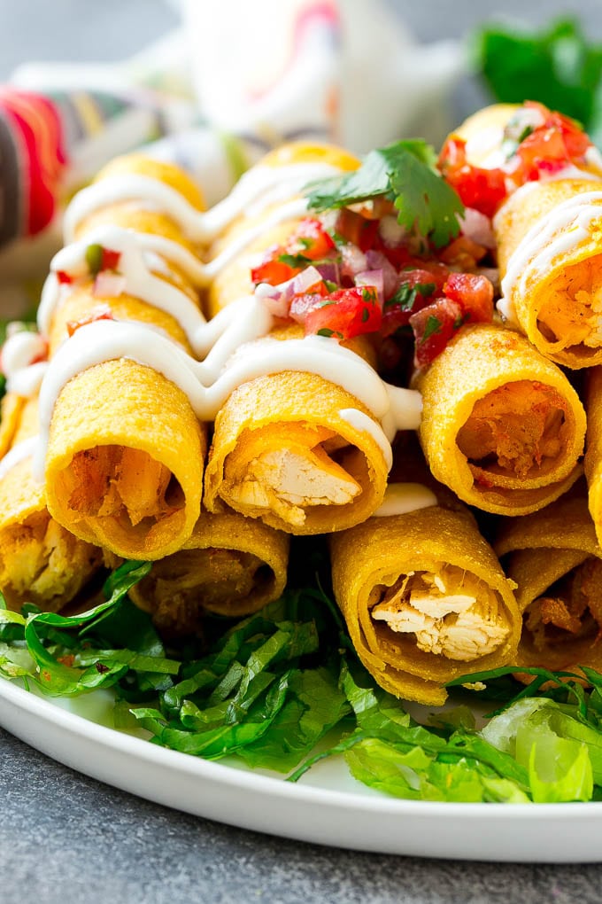 Chicken Taquitos Recipe | Baked Chicken Taquitos | Fried Chicken Taquitos | Mexican Appetizer | Chicken Tortillas #taquitos #chicken #appetizer #tortillas #mexicanfood #sraye A plate of chicken taquitos on a bed of lettuce, topped with sour cream and pico de gallo.