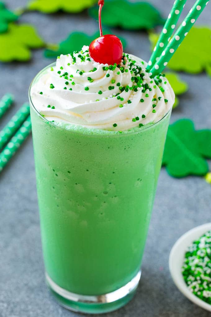 Shamrock Shake Recipe | McDonald's Shamrock Shake | Saint Patrick's Day Drink | Mint Milkshake #milkshake #stpatricksday #saintpatricksday #mint #sraye A glass of shamrock shake topped with whipped cream, sprinkles and a cherry.