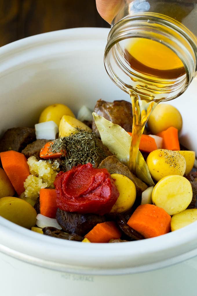 Slow Cooker Beef Stew Recipe | Crockpot Beef Stew #stew #soup #beef #slowcooker #crockpot #dinner #sraye Broth being poured into a slow cooker filled with beef and vegetables.