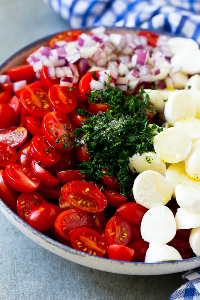 Cherry Tomato Salad Recipe | Tomato Mozzarella Salad | Caprese Salad | Tomato Salad #tomatoes #salad #tomatosalad #caprese #sraye Cherry tomatoes, herbs, mozzarella balls and red onion drizzled with dressing in a bowl.