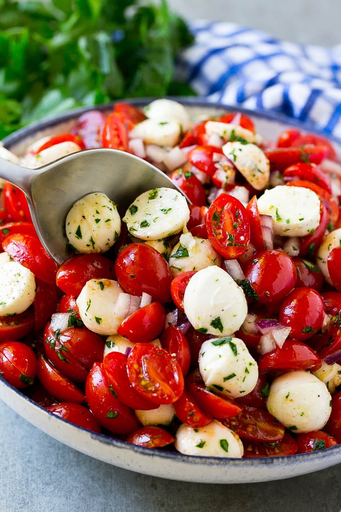 Cherry Tomato Salad Recipe | Tomato Mozzarella Salad | Caprese Salad | Tomato Salad #tomatoes #salad #tomatosalad #caprese #sraye A bowl of cherry tomato salad with a serving spoon in it.