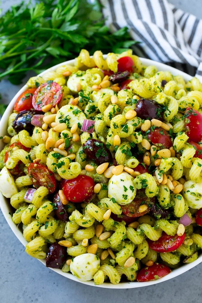 Pesto Pasta Salad | Italian Pasta Salad | Easy Pasta Salad #pasta #salad #pesto #olives #tomatoes #sraye A bowl of pesto pasta salad topped with pine nuts and chopped parsley.