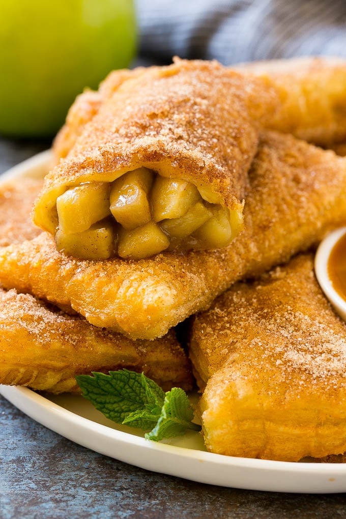 Fried Apple Pies Recipe | McDonald's Copycat Recipe | Apple Pie | Apple Hand Pies #pie #apples #applepie #dessert #snack #sraye Fried apple pies on a plate served with caramel sauce and topped with cinnamon sugar.