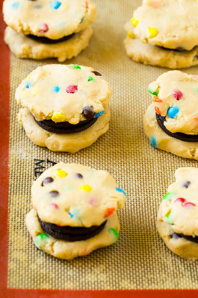 Oreo Stuffed Cookies Recipe | M&M's cookies | Stuffed Cookies #cookies #chocolate #oreos #dessert #baking #sraye Cookie dough sandwiched around Oreos on a baking sheet.