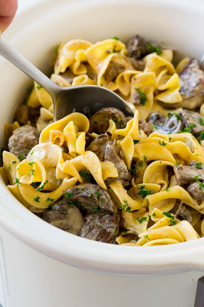 Slow Cooker Beef Stroganoff Recipe | Crock Pot Beef Stroganoff | Beef Recipe #slowcooker #crockpot #beef #mushrooms #pasta #dinner #sraye A crock pot of beef stroganoff with a serving spoon in it.