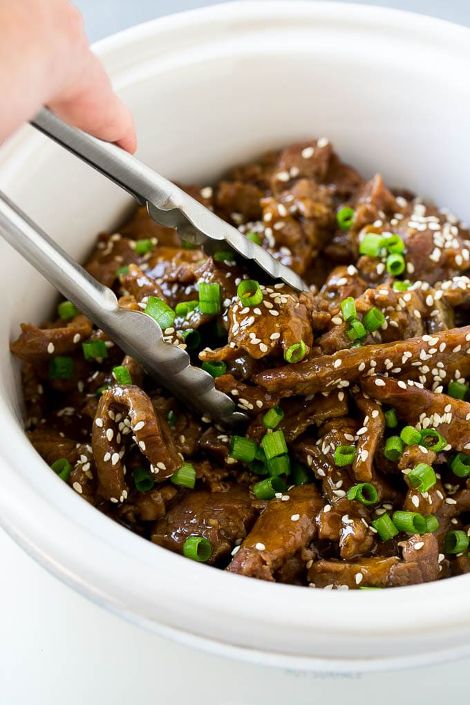 Slow Cooker Korean Beef Recipe | Korean Beef | Flank Steak Recipe #dinner #beef #slowcooker #crockpot #asian #sraye A crock pot of Korean beef with serving tongs in it.