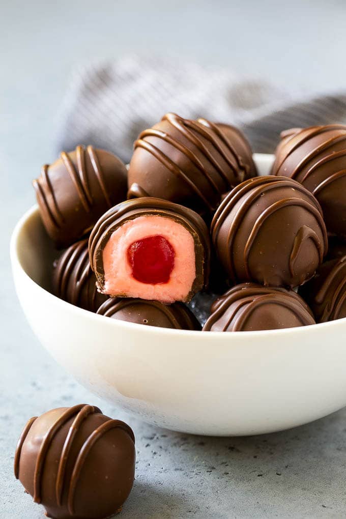 Chocolate Covered Cherries Recipe | Cherry Cordials | Cherry Candy #chocolate #candy #dessert #cherry #sweets #sraye A bowl of chocolate covered cherries with one cut open.