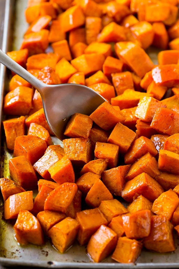 Maple Roasted Sweet Potatoes Recipe | Easy Sweet Potatoes | Baked Sweet Potatoes | Sweet Potato Side Dish #sweetpotatoes #cinnamon #maple #butter #fall #sidedish #dinner #sraye A sheet pan of baked yams flavored with maple and cinnamon, with a serving spoon in them.