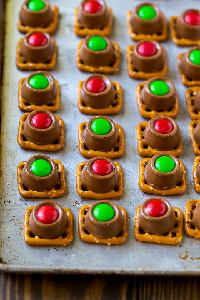 Rolo Pretzels Recipe | Chocolate Pretzels | Caramel Pretzels | Holiday Candy #christmas #baking #dessert #candy #chocolate #caramel #pretzels #sraye Treats with red and green M&M's pressed on top all on a baking sheet.