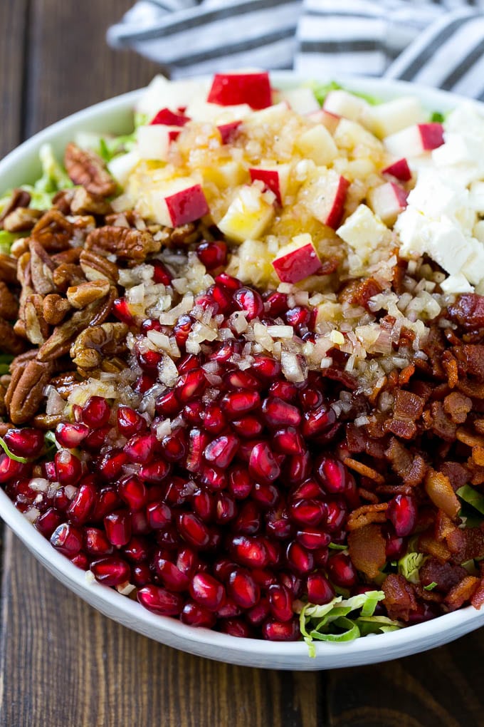 Brussels Sprout Salad Recipe | Shredded Brussels Sprouts Salad | Fall Salad #salad #brusselssprouts #bacon #thanksgiving #pomegranate #apple #dinner #sraye Dressing poured on top of salad that contains sprouts, pomegranate seeds, pecans and bacon.