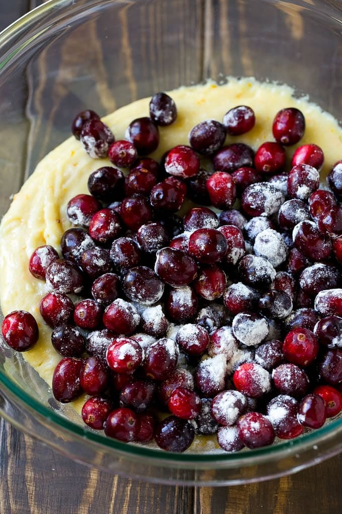 Cranberry Bread Recipe | Cranberry Loaf | Cranberry Orange Bread #cranberry #bread #baking #dessert #fall #sraye Orange batter topped with a pile of fresh cranberries in a mixing bowl.