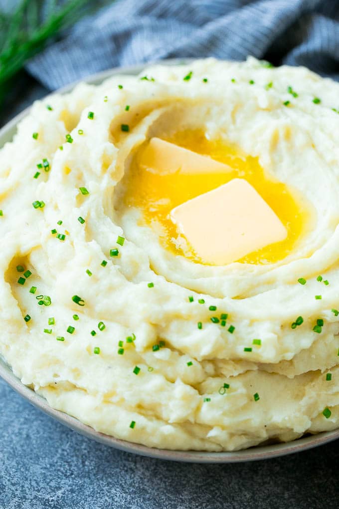 Instant Pot Mashed Potatoes Recipe | Pressure Cooker Mashed Potatoes | Easy Mashed Potatoes #potatoes #sidedish #instantpot #thanksgiving #dinner #sraye A bowl of fluffy Instant Pot mashed potatoes topped with pats of butter and sliced chives.