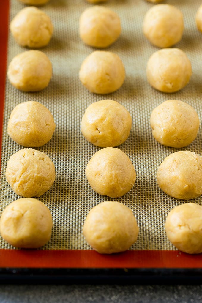 Peanut Butter Blossoms Recipe | Hershey Kiss Cookies | Chocolate Peanut Butter Cookies #cookies #peanutbutter #chocolate #dessert #baking #christmas #christmascookies #sraye Balls of dough on a baking sheet.