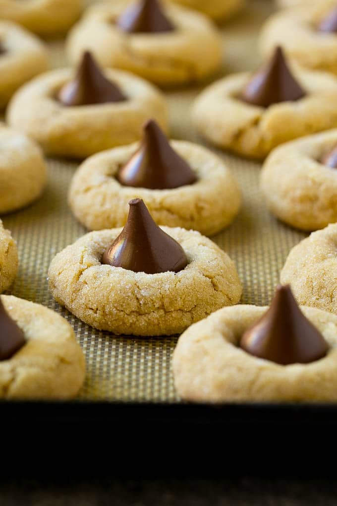 Peanut Butter Blossoms Recipe | Hershey Kiss Cookies | Chocolate Peanut Butter Cookies #cookies #peanutbutter #chocolate #dessert #baking #christmas #christmascookies #sraye Baked peanut butter blossom cookies on a sheet pan.