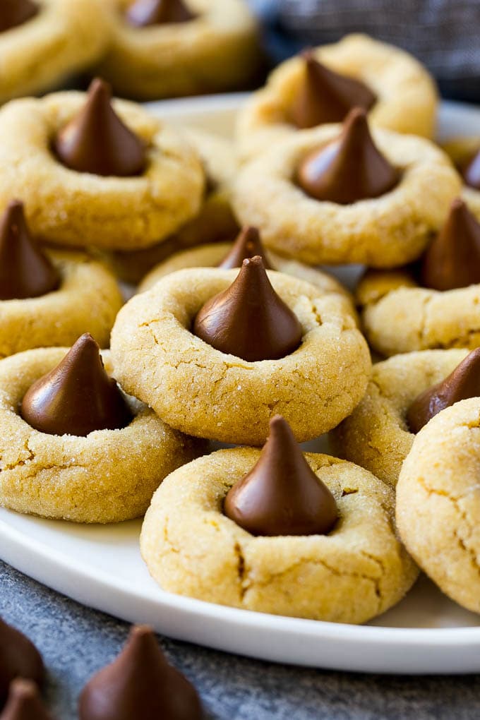 Peanut Butter Blossoms Recipe | Hershey Kiss Cookies | Chocolate Peanut Butter Cookies #cookies #peanutbutter #chocolate #dessert #baking #christmas #christmascookies #sraye A plate with peanut butter blossoms stacked onto it.