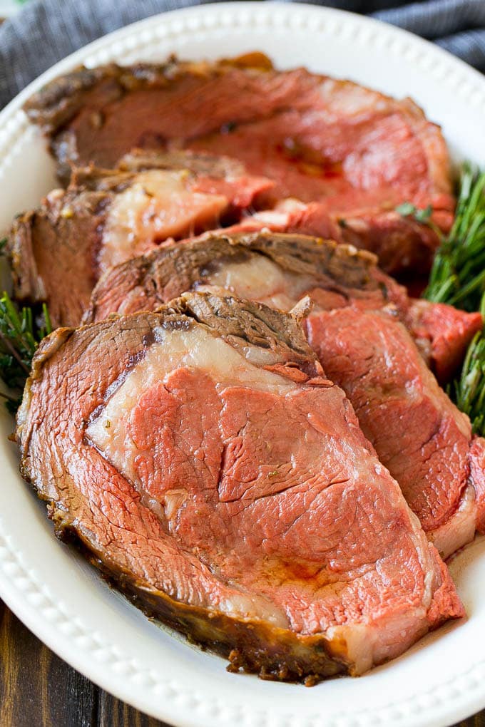 Smoked Prime Rib Recipe | Easy Prime Rib | Smoked Beef | Holiday Prime Rib #primerib #beef #smoker #dinner #sraye #christmas #thanksgiving #lowcarb #keto Slices of beef garnished with fresh herbs.