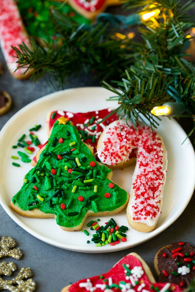 Christmas Sugar Cookies Recipe | Christmas Cookies #cookies #frosting #sprinkles #sugarcookies #christmas #dessert #sraye A selection of Christmas sugar cookies served on a plate, with holiday decorations in the background.
