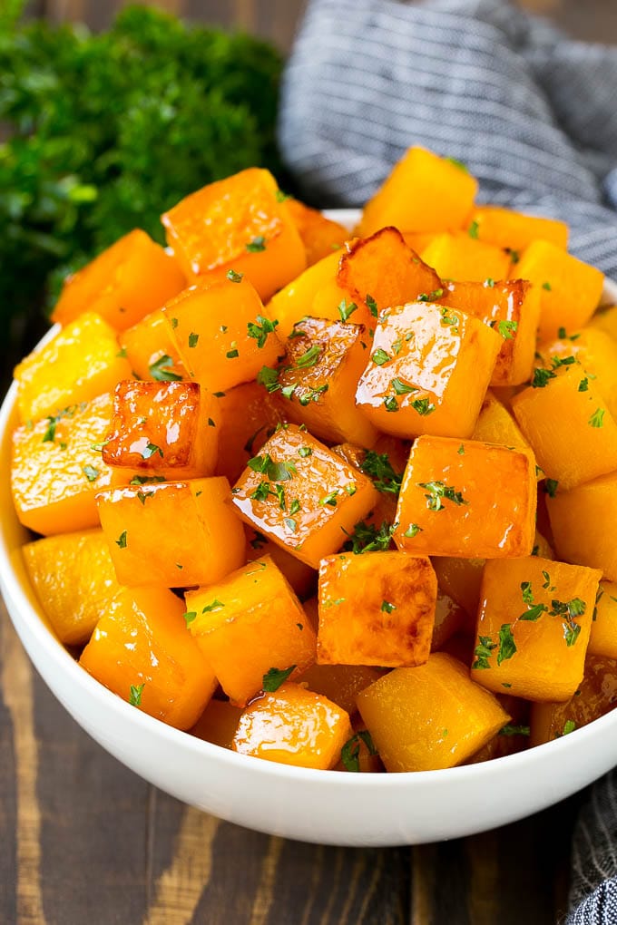 Roasted Butternut Squash Recipe | Baked Butternut Squash | Butternut Squash Side Dish #butternutsquash #squash #fall #vegetarian #dinner #sraye A bowl of roasted butternut squash made with brown sugar and maple syrup, then garnished with chopped parsley.