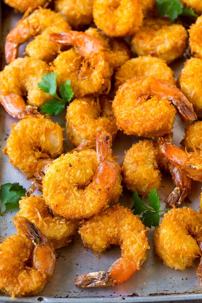 Coconut Shrimp Recipe | Fried Shrimp | Shrimp Appetizer #shrimp #coconut #appetizer #seafood #dinner #sraye A pile of crispy coconut shrimp on a sheet pan with cilantro leaves for garnish.