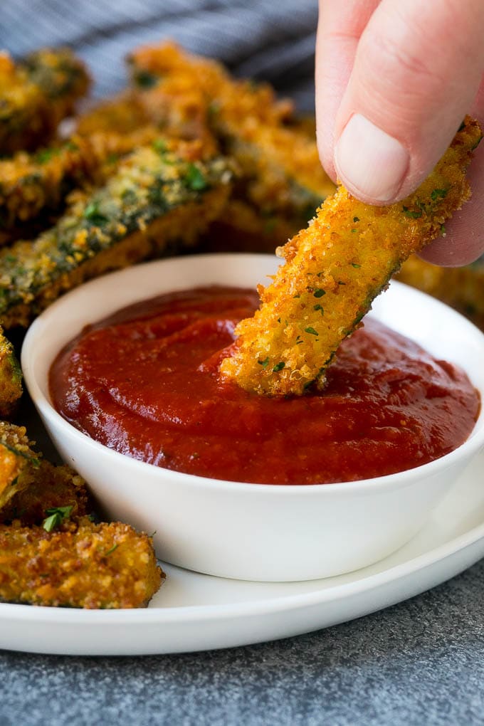 Fried Zucchini Recipe | Zucchini Fries | Zucchini Recipe #appetizer #zucchini #snack #sraye A hand dipping a piece of fried zucchini into marinara sauce.