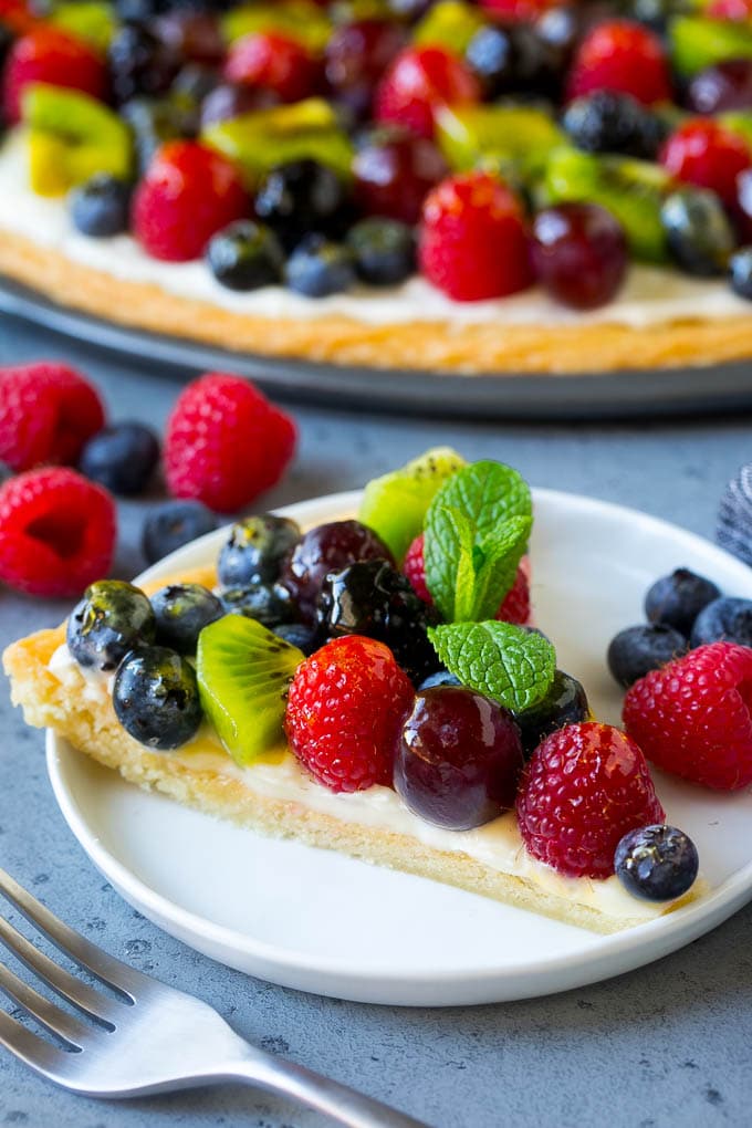Fruit Pizza Recipe | Dessert Pizza | Fruit Dessert #cookie #fruit #pizza #dessert #sweets #sraye A slice of fruit pizza topped with cream cheese frosting and berries.
