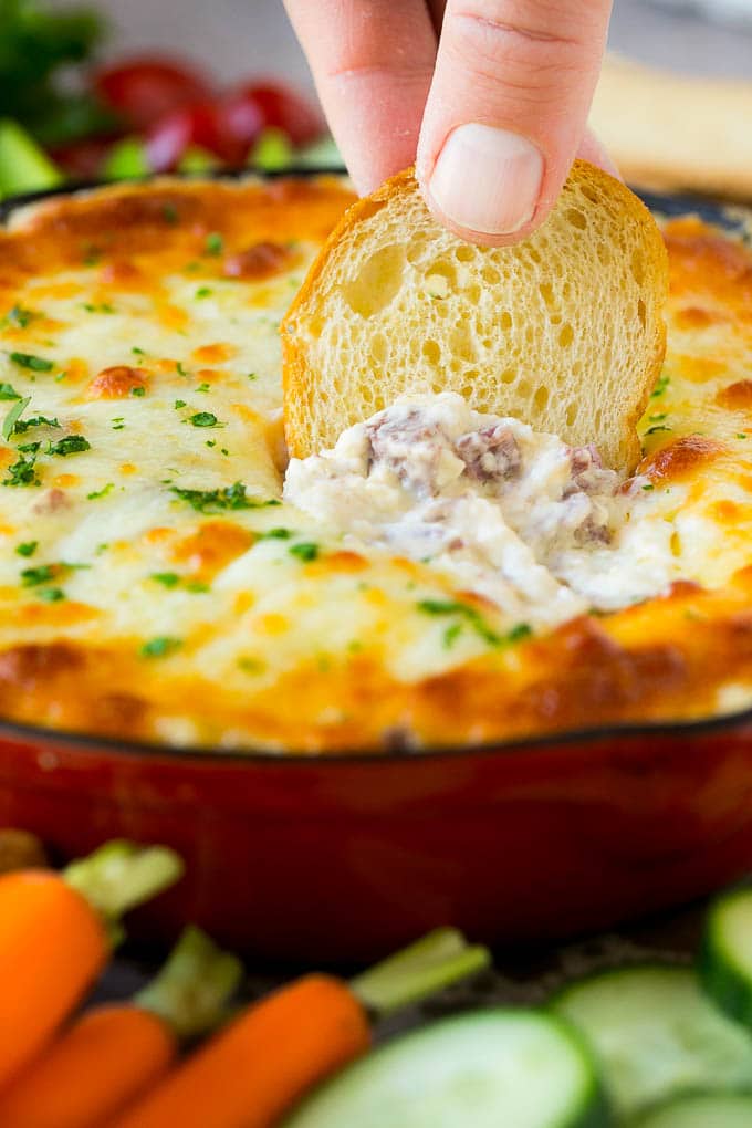 Reuben Dip Recipe | Corned Beef Dip | Cheese Dip #dip #cheese #cornedbeef #appetizer #lowcarb #keto #sraye A baguette chip dipping into a skillet of Reuben dip.