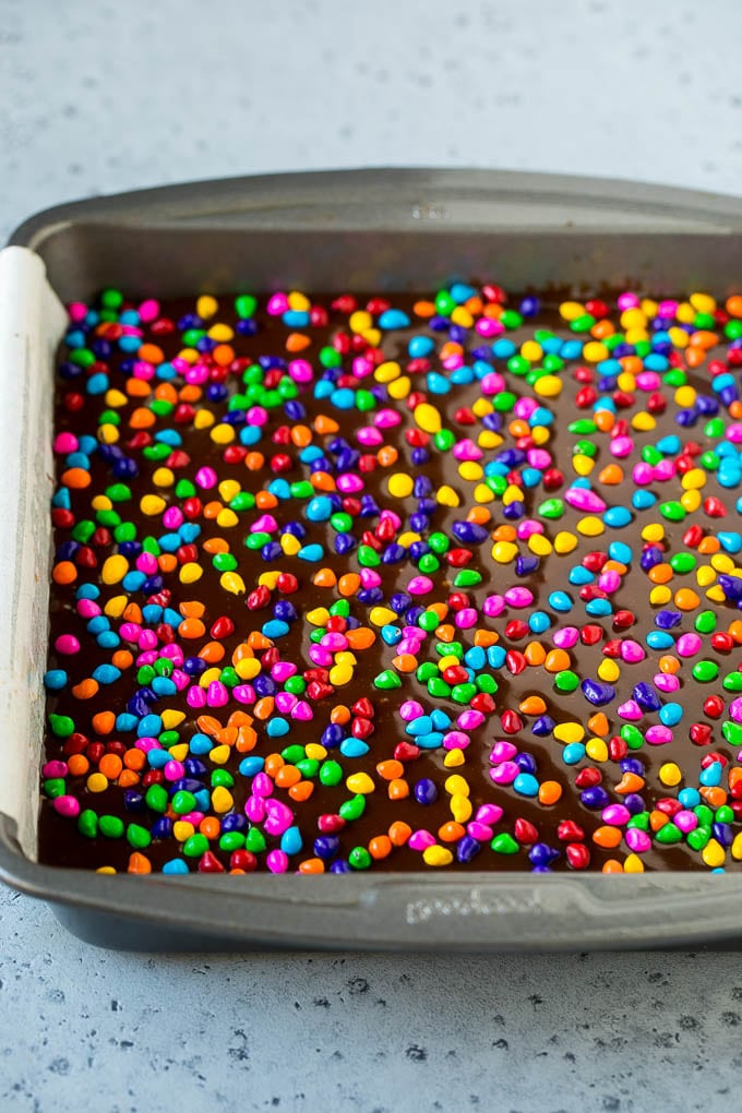 Cosmic Brownies Recipe | Cocoa Brownies | Frosted Brownies #brownies #chocolate #dessert #sraye #sprinkles A pan of cosmic brownies with rainbow sprinkles on top.