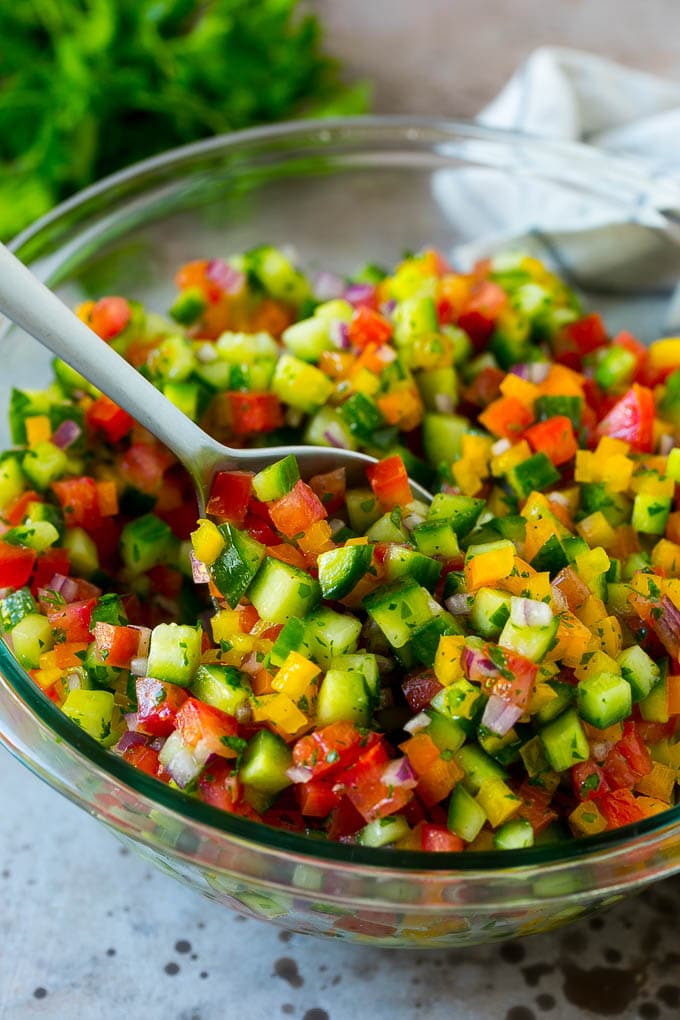 Israeli Salad Recipe | Cucumber Salad | Tomato Salad | Chopped Salad #salad #cleaneating #healthy #glutenfree #lowcarb #keto #sidedish #lunch #sraye A bowl of Israeli salad with a serving spoon in it.