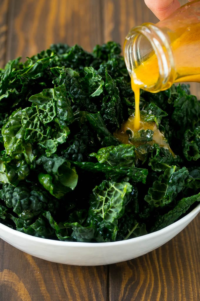 Apple Kale Salad Recipe | Kale Recipe | Fall Salad #kale #apples #bacon #salad #feta #dinner #lunch #sraye Dressing being poured over dinosaur kale leaves.
