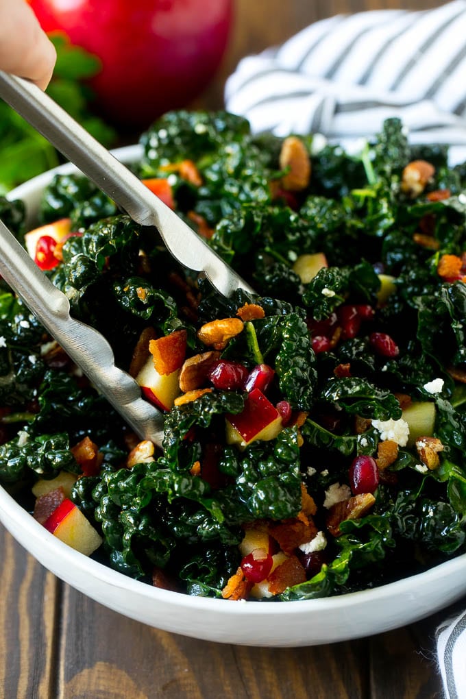 Apple Kale Salad Recipe | Kale Recipe | Fall Salad #kale #apples #bacon #salad #feta #dinner #lunch #sraye Tongs in a bowl of kale and apple salad.