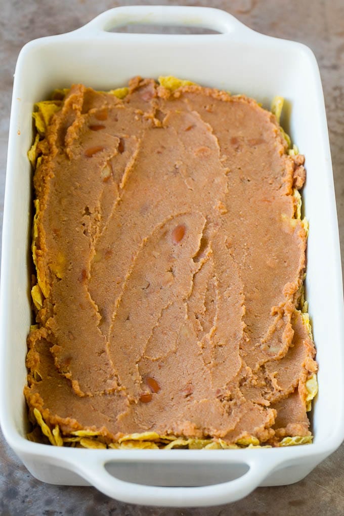 Taco Casserole Recipe | Mexican Casserole | Beef Casserole #casserole #tacos #beef #dinner #cheese #sraye A layer of refried beans on top of a crushed tortilla chips.
