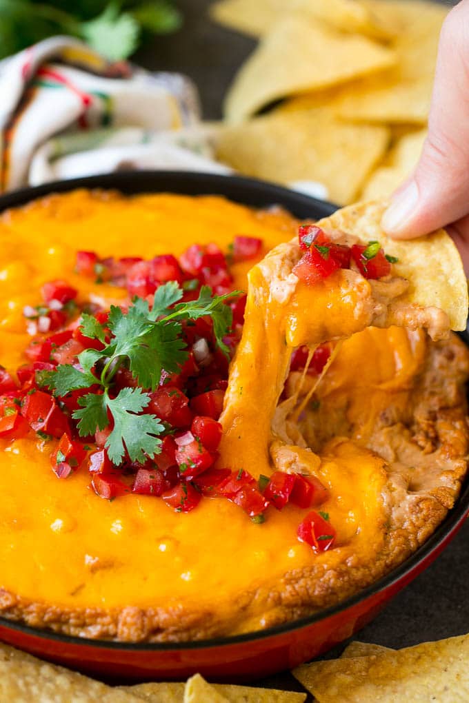 Bean Dip Recipe | Mexican Dip #dip #appetizer #mexicanfood #beans #cheese #sraye A tortilla chip scooping out a serving of Mexican bean dip.