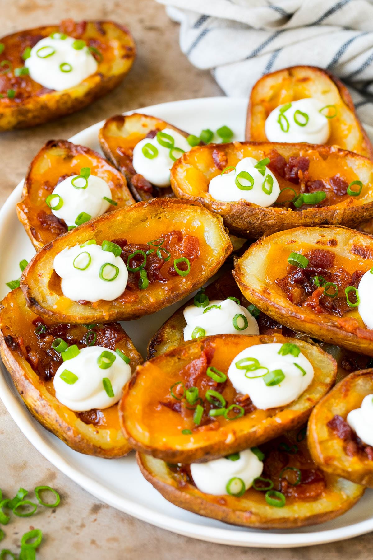 Potato Skins Recipe | Loaded Potatoes #potatoes #appetizer #snack #cheese #bacon #sraye A serving plate of potato skins topped with bacon and sour cream.