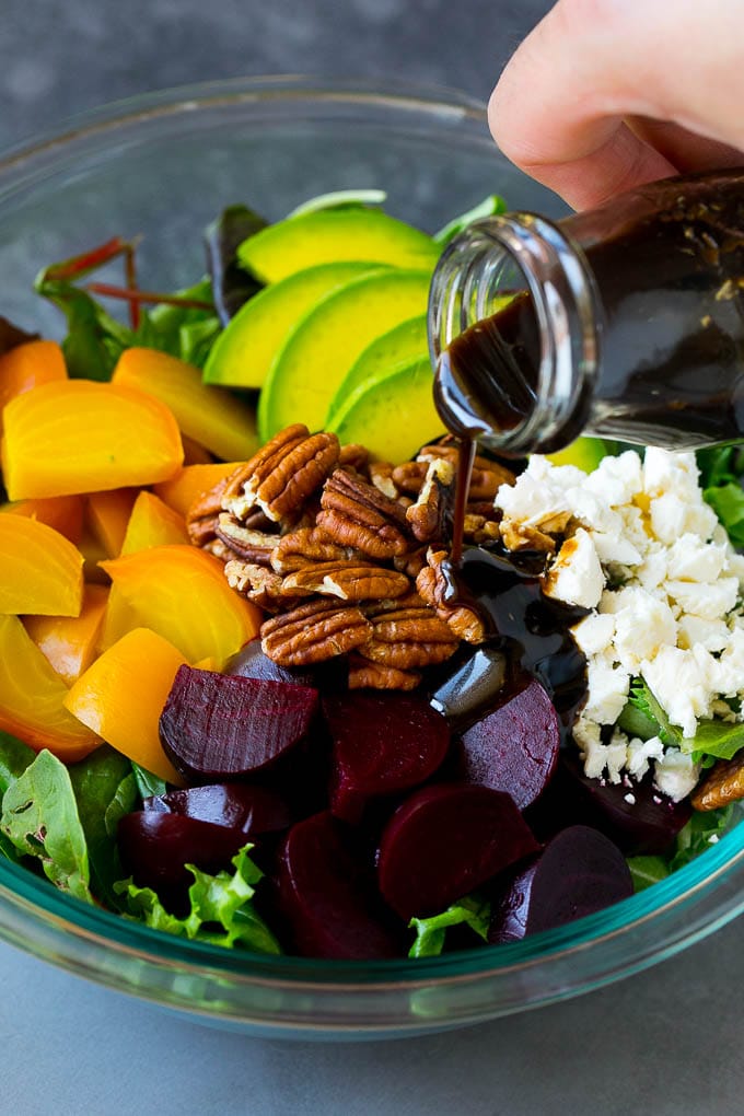 Beet Salad Recipe #beets #avocado #feta #salad #dinner #sraye Balsamic dressing being poured over beets, sliced avocado and feta cheese.