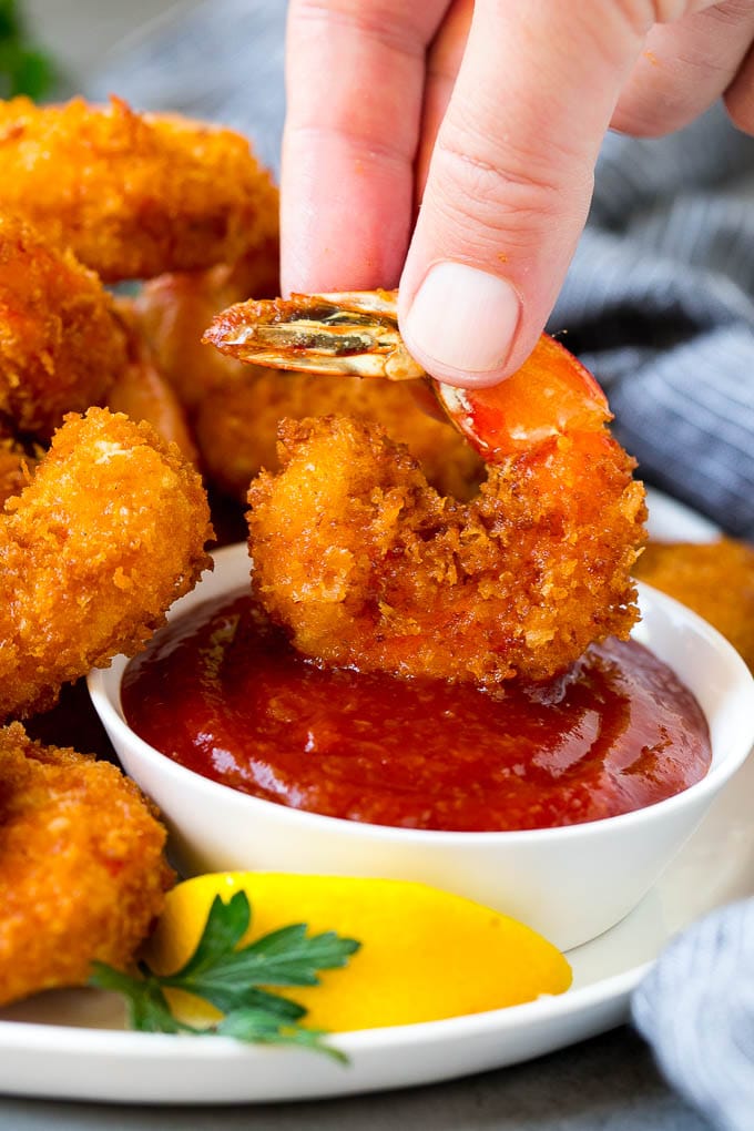 Fried Shrimp Recipe #shrimp #seafood #dinner #appetizer #sraye A hand dipping a shrimp into cocktail sauce.