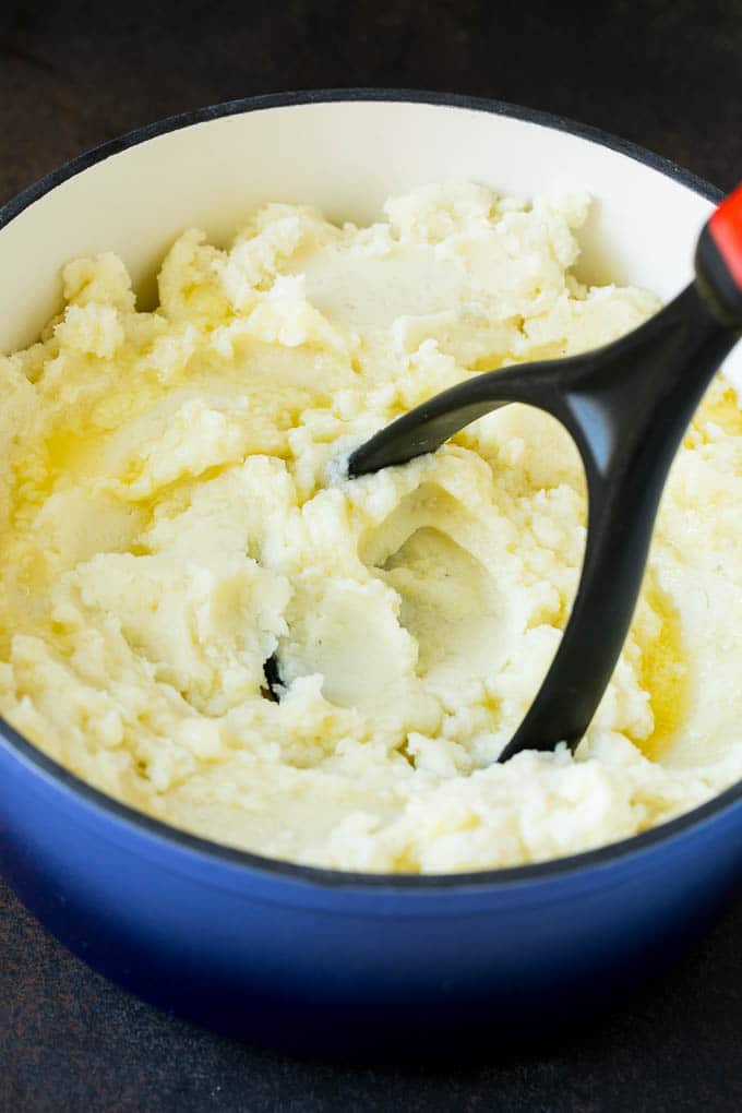 Garlic Mashed Potatoes Recipe #garlic #potatoes #mashedpotatoes #sidedish #dinner #thanksgiving #sraye A potato masher smashing diced cooked potatoes.