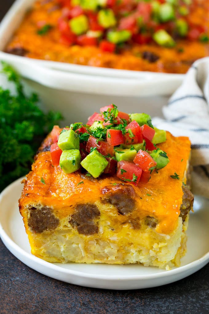 Sausage Egg Casserole Recipe | Egg Casserole #eggs #sausage #potato #cheese #casserole #breakfast #brunch #sraye A slice of sausage egg casserole with a garnish of fresh tomatoes.