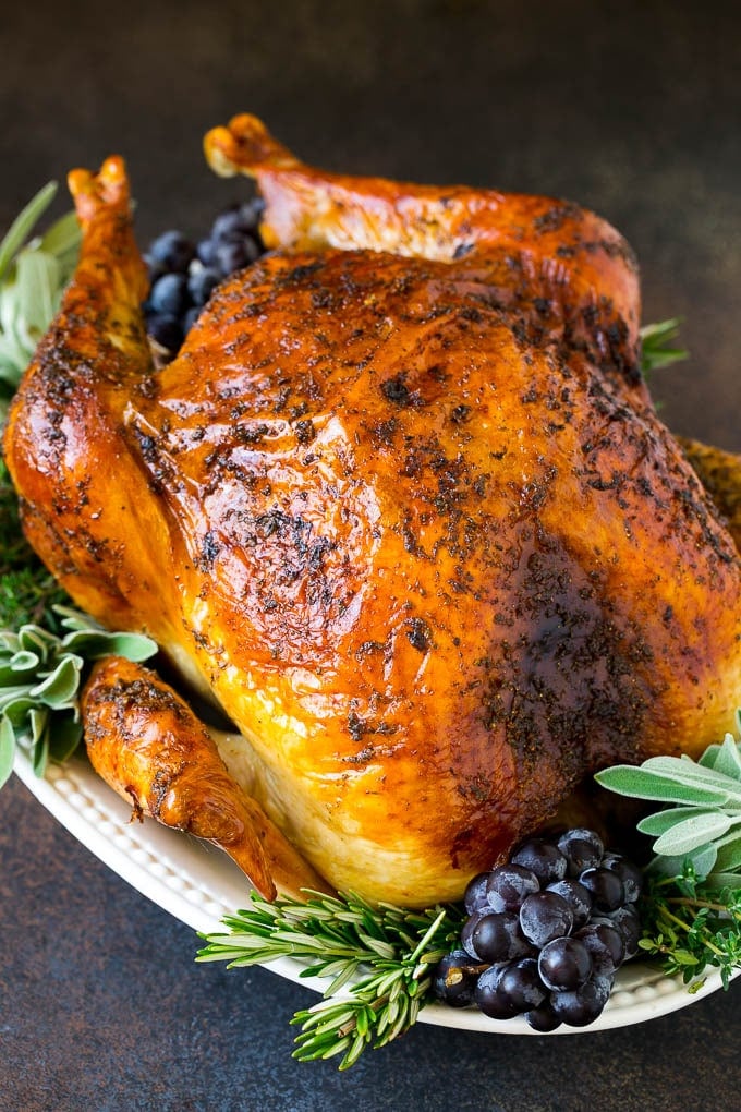 Thanksgiving Turkey Recipe | Roasted Turkey #turkey #thanksgiving #fall #dinner #sraye A whole roasted Thanksgiving turkey on a platter that's decorated with grapes and herbs.